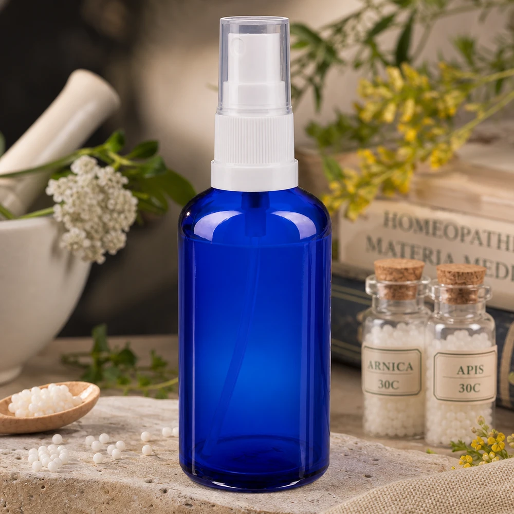 Flacon pulvérisateur en verre d'apothicaire bleu de 50 ml muni d'une pompe blanche, à côté de granules homéopathiques